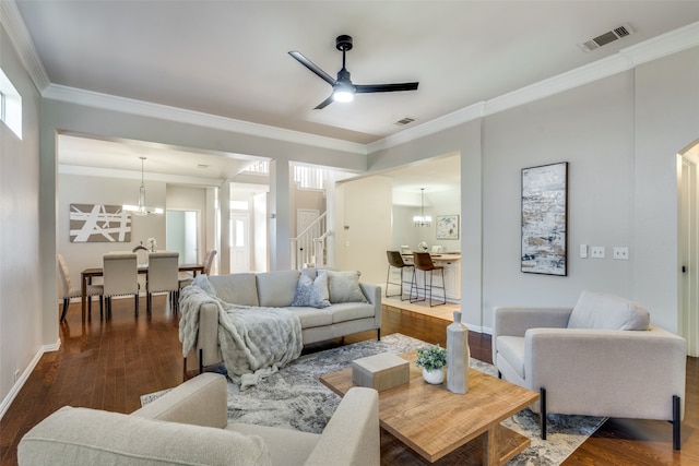 living room with ceiling fan with notable chandelier, ornamental molding, and dark wood-type flooring