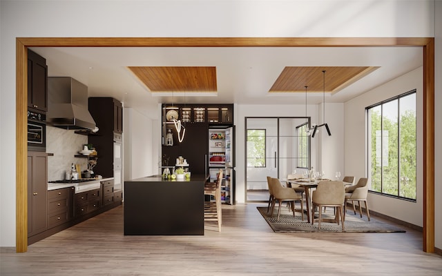 interior space featuring appliances with stainless steel finishes, wall chimney exhaust hood, decorative light fixtures, and light wood-type flooring