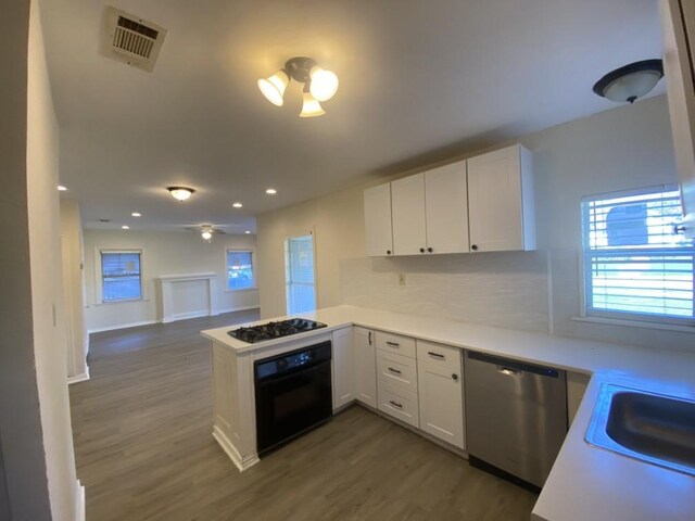 kitchen featuring kitchen peninsula, dark hardwood / wood-style flooring, stainless steel dishwasher, white cabinets, and black oven