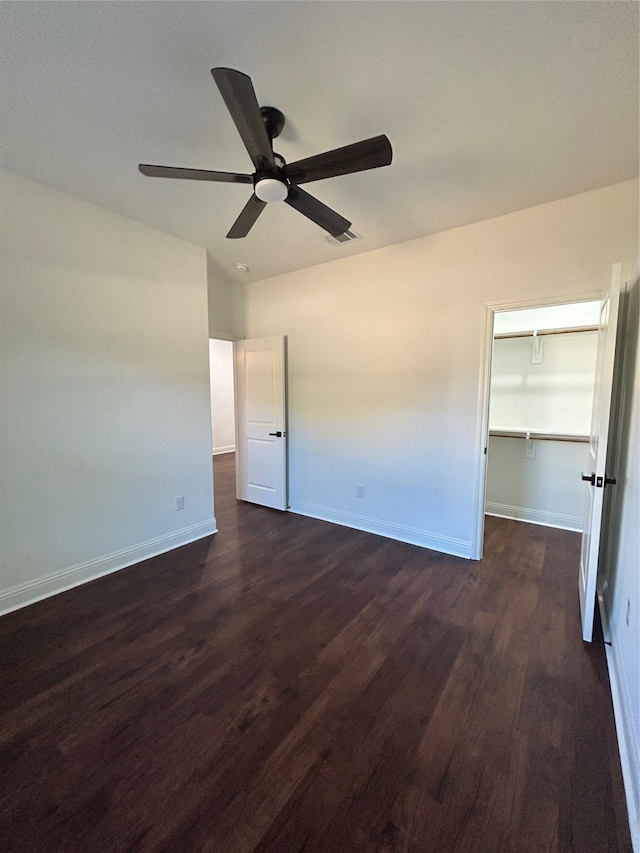 unfurnished bedroom featuring a closet, a spacious closet, ceiling fan, and dark wood-type flooring