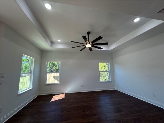 spare room with a raised ceiling, ceiling fan, dark hardwood / wood-style flooring, and a healthy amount of sunlight