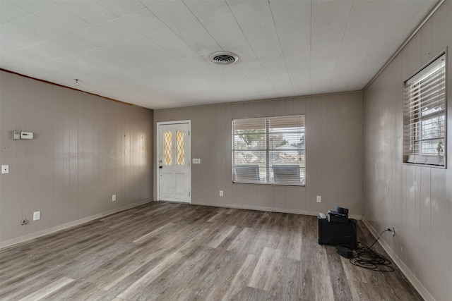 unfurnished room with light wood-type flooring, crown molding, and wooden walls