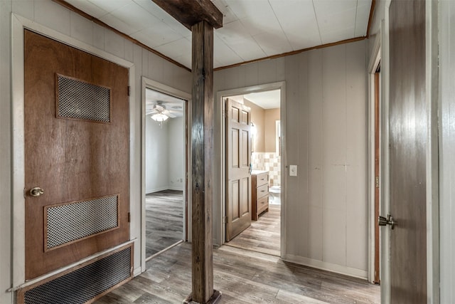 corridor with wood walls, light wood-type flooring, and crown molding