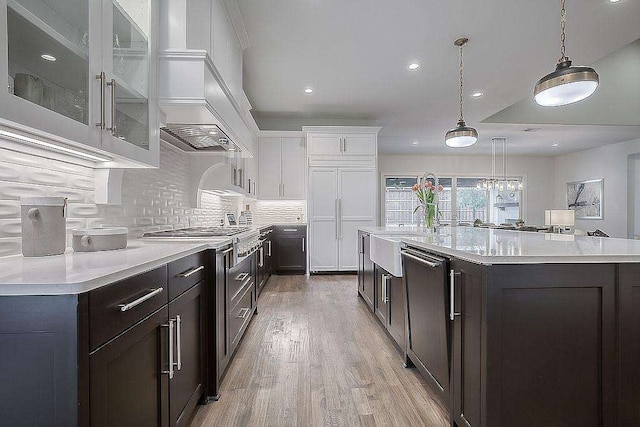 kitchen with pendant lighting, white cabinets, a center island with sink, light wood-type flooring, and stainless steel appliances