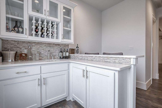 bar with decorative backsplash, dark hardwood / wood-style flooring, white cabinets, and sink