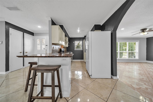 kitchen featuring white refrigerator, light tile patterned floors, a textured ceiling, ornamental molding, and white cabinetry