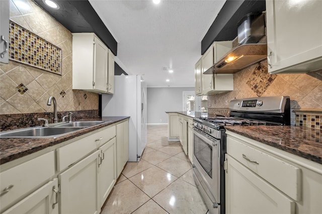 kitchen featuring tasteful backsplash, stainless steel gas range, wall chimney range hood, sink, and light tile patterned floors