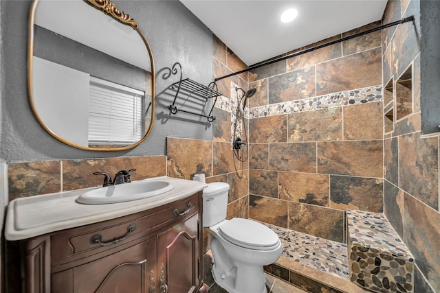 bathroom with a tile shower, vanity, toilet, and tile walls