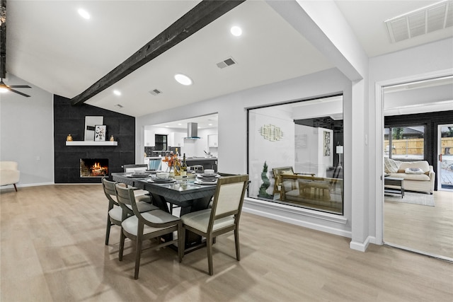 dining room with vaulted ceiling with beams, ceiling fan, light hardwood / wood-style flooring, and a tile fireplace