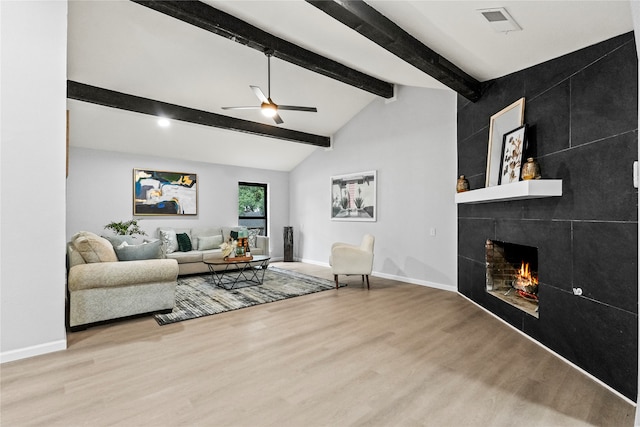 living room with vaulted ceiling with beams, ceiling fan, a tile fireplace, and light wood-type flooring