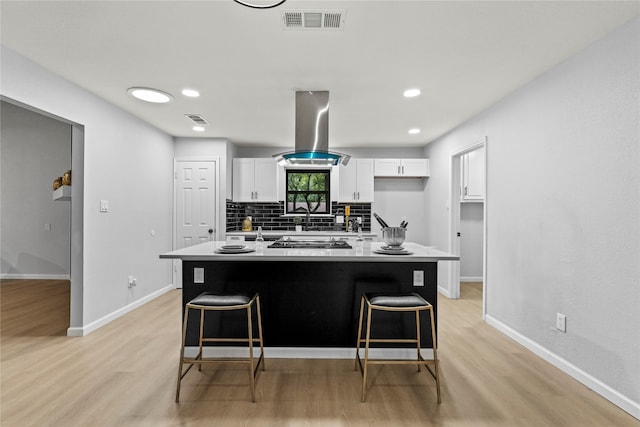 kitchen with white cabinetry, island exhaust hood, a breakfast bar area, and light hardwood / wood-style flooring