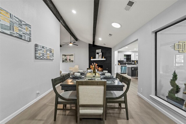 dining room with a tiled fireplace, ceiling fan, lofted ceiling with beams, and wood-type flooring