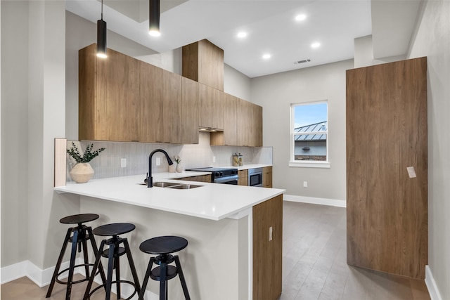 kitchen featuring a kitchen bar, kitchen peninsula, light wood-type flooring, stainless steel electric stove, and sink