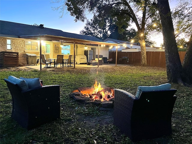 back house at dusk featuring a lawn, ceiling fan, a patio, and an outdoor fire pit