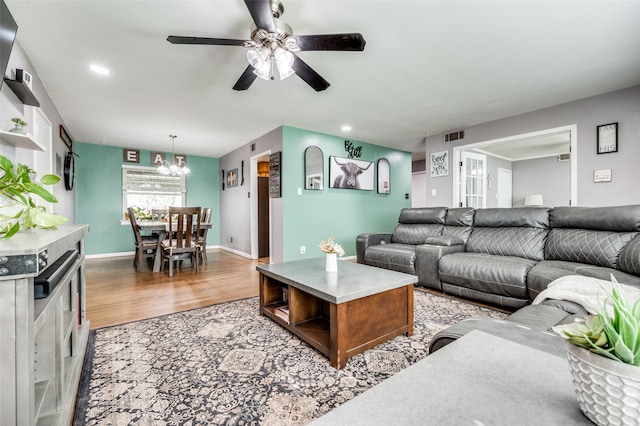 living room featuring ceiling fan with notable chandelier and light wood-type flooring