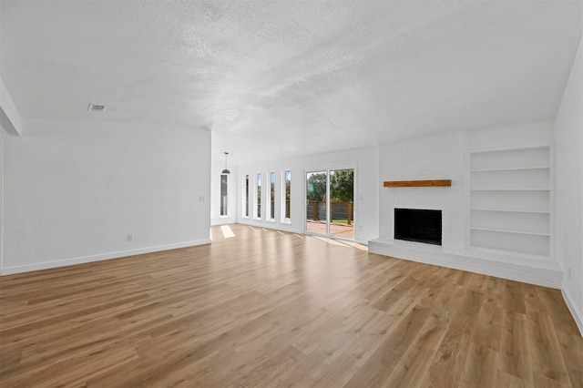 unfurnished living room with built in features, a brick fireplace, a textured ceiling, and light hardwood / wood-style flooring