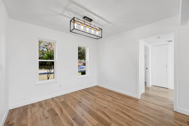 unfurnished room featuring a chandelier, a textured ceiling, and light hardwood / wood-style floors