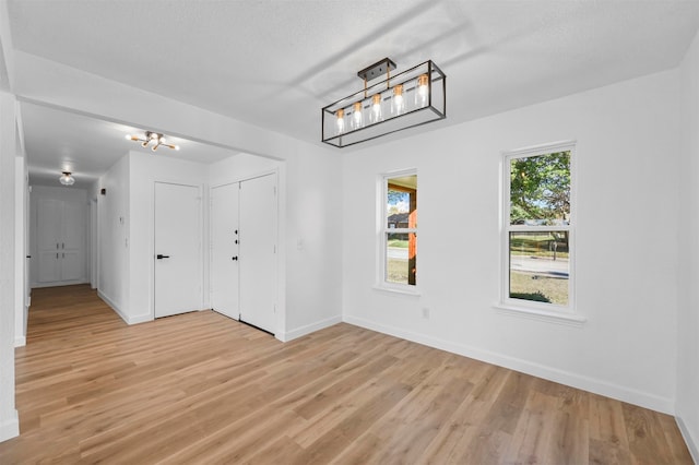 spare room with a textured ceiling, light hardwood / wood-style flooring, and a notable chandelier