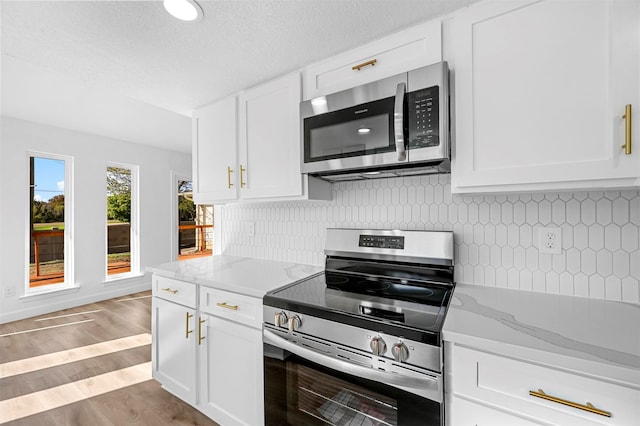 kitchen with white cabinets, a textured ceiling, appliances with stainless steel finishes, light hardwood / wood-style floors, and light stone counters