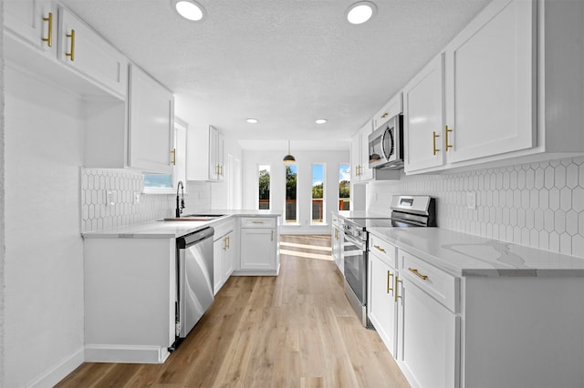 kitchen featuring white cabinetry, sink, stainless steel appliances, light hardwood / wood-style floors, and pendant lighting