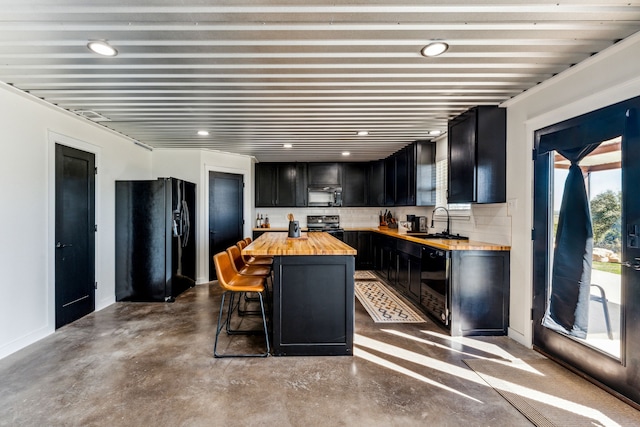 kitchen with a center island, wood counters, concrete floors, a kitchen bar, and black appliances