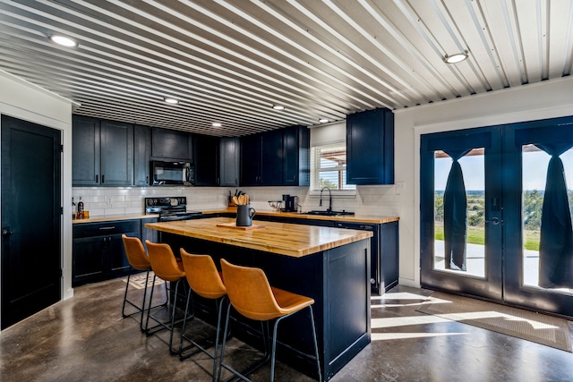 kitchen with butcher block countertops, a center island, a kitchen bar, and black appliances