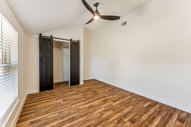 unfurnished bedroom with a barn door, hardwood / wood-style flooring, vaulted ceiling, and ceiling fan