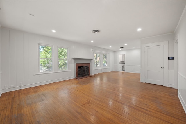 unfurnished living room featuring a brick fireplace, light hardwood / wood-style floors, and ornamental molding