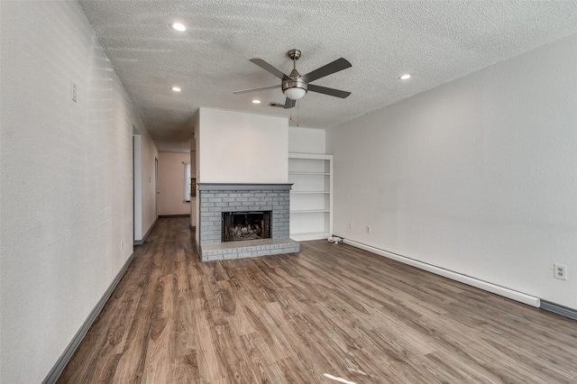 unfurnished living room with a brick fireplace, hardwood / wood-style flooring, ceiling fan, a textured ceiling, and a baseboard radiator