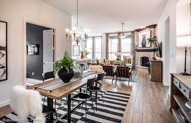 dining area with a notable chandelier, a stone fireplace, and light hardwood / wood-style flooring