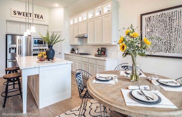 kitchen with stainless steel appliances, decorative light fixtures, white cabinets, hardwood / wood-style floors, and an island with sink