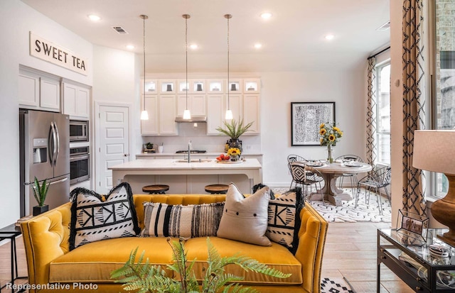 kitchen with a kitchen bar, stainless steel appliances, a center island with sink, light hardwood / wood-style floors, and white cabinetry