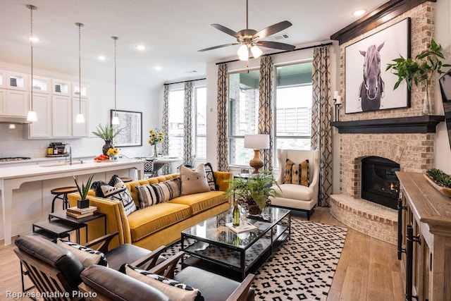 living room featuring a fireplace, light wood-type flooring, ceiling fan, and sink