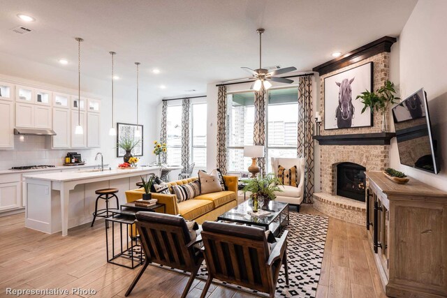 living room with a fireplace, light hardwood / wood-style flooring, ceiling fan, and sink