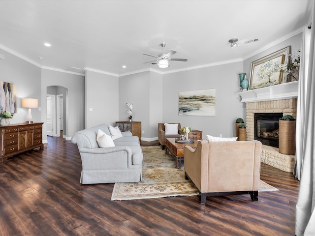 living room with dark hardwood / wood-style floors, ceiling fan, ornamental molding, and a brick fireplace