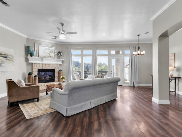 living room featuring a brick fireplace, ornamental molding, a textured ceiling, ceiling fan with notable chandelier, and dark hardwood / wood-style floors