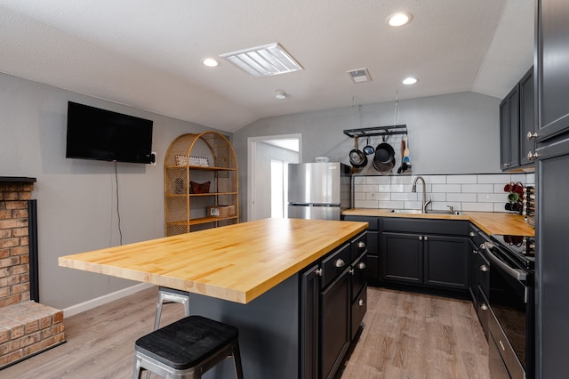 kitchen featuring butcher block countertops, stainless steel fridge, a kitchen bar, and range with electric cooktop