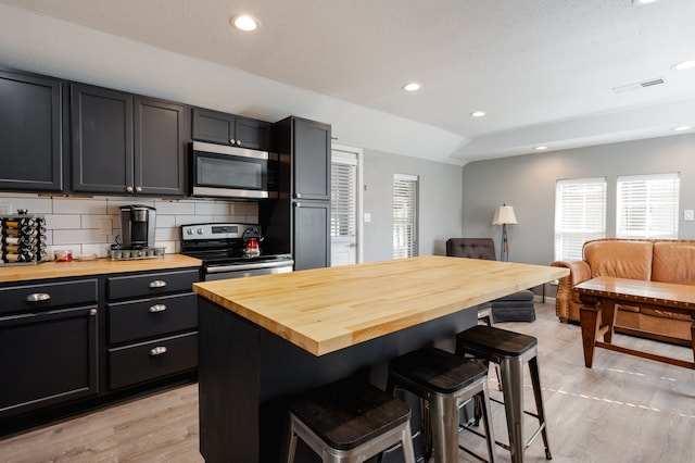 kitchen featuring a center island, a kitchen bar, appliances with stainless steel finishes, and wooden counters