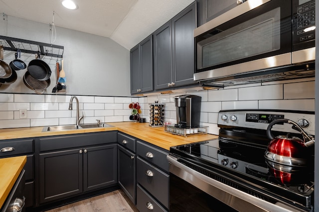 kitchen with sink, stainless steel appliances, light hardwood / wood-style flooring, butcher block countertops, and vaulted ceiling