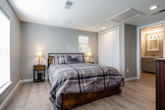 bedroom with ensuite bathroom, a closet, and light hardwood / wood-style flooring