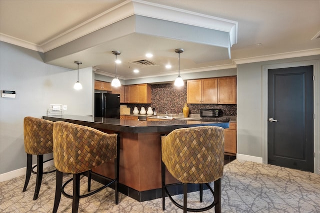 kitchen featuring pendant lighting, a breakfast bar, black fridge, ornamental molding, and kitchen peninsula