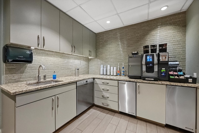 kitchen with sink, a drop ceiling, stainless steel appliances, light stone counters, and light hardwood / wood-style flooring