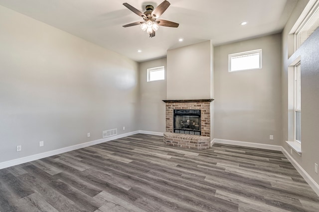 unfurnished living room featuring a fireplace, dark hardwood / wood-style floors, ceiling fan, and a healthy amount of sunlight