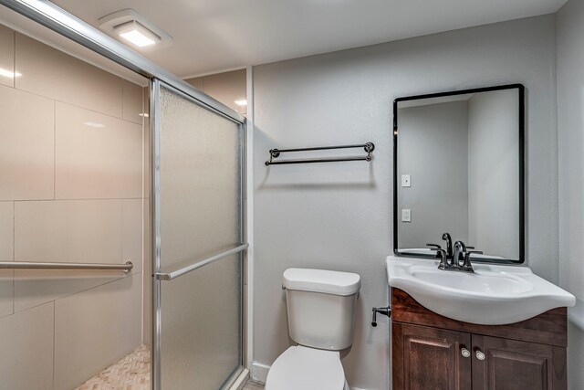 bathroom featuring a shower with door, vanity, and toilet