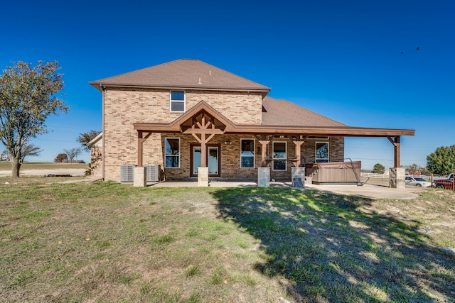 rear view of property with a lawn, cooling unit, a patio, and a hot tub