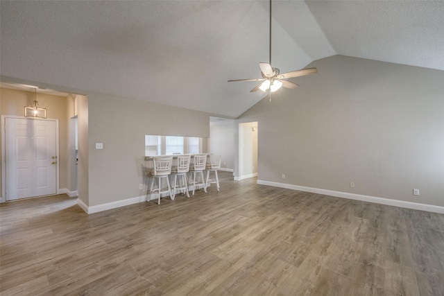 unfurnished living room featuring ceiling fan, light wood-type flooring, a textured ceiling, and vaulted ceiling