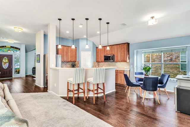 kitchen featuring stainless steel appliances, tasteful backsplash, dark hardwood / wood-style floors, pendant lighting, and a kitchen bar