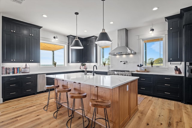 kitchen featuring a wealth of natural light, a kitchen island with sink, light hardwood / wood-style floors, and wall chimney range hood