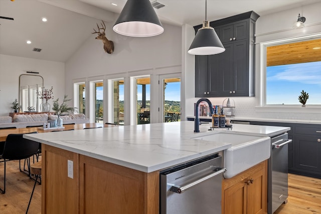 kitchen featuring light stone counters, pendant lighting, a kitchen island with sink, and light hardwood / wood-style floors