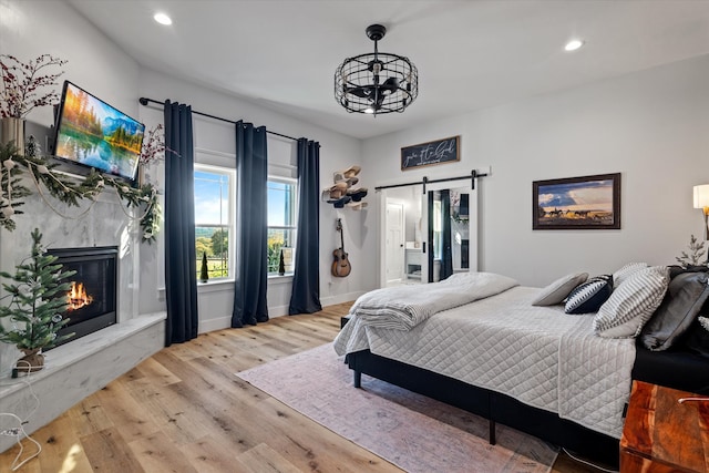 bedroom featuring ensuite bath, a premium fireplace, light hardwood / wood-style floors, and a barn door